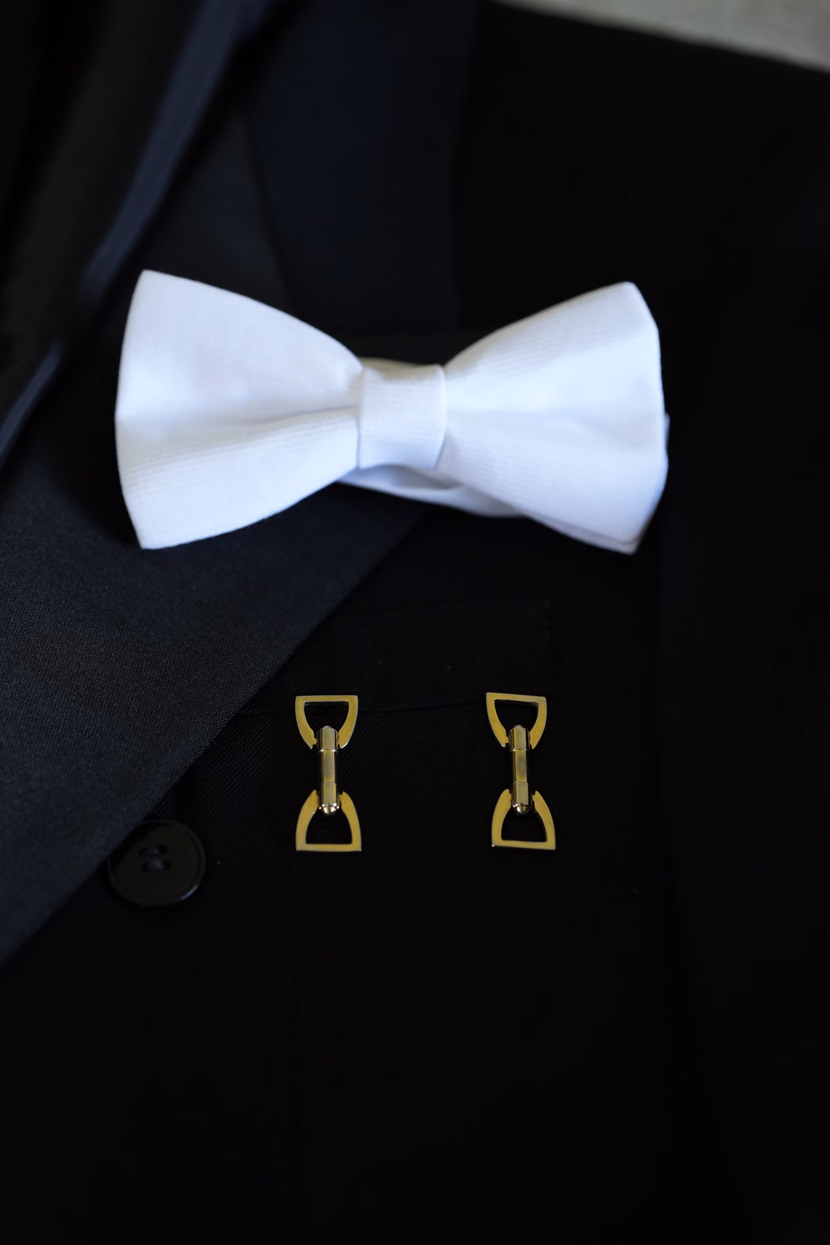 Moño blanco y mancornas doradas sobre el traje negro del novio