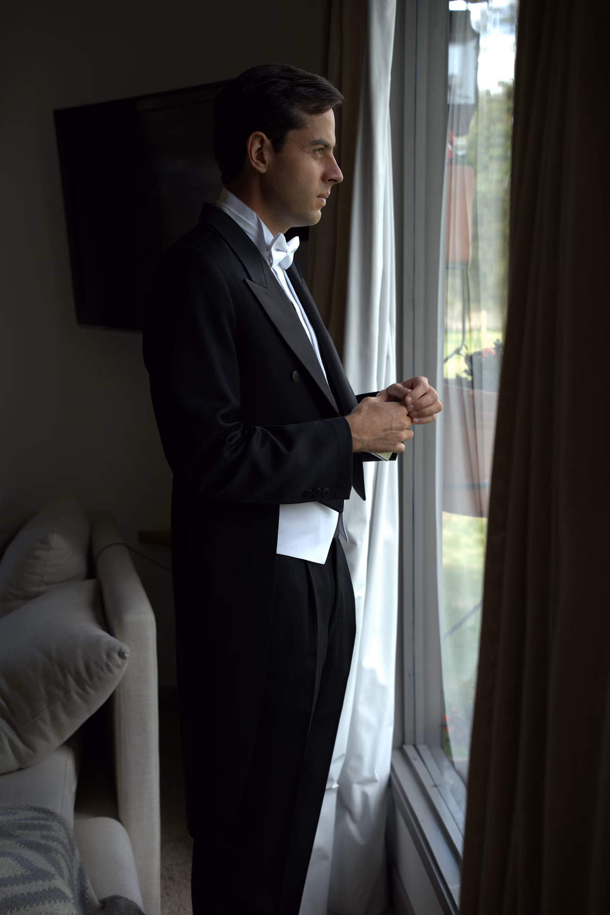 Novio vestido de gala junto a una ventana antes de la boda
