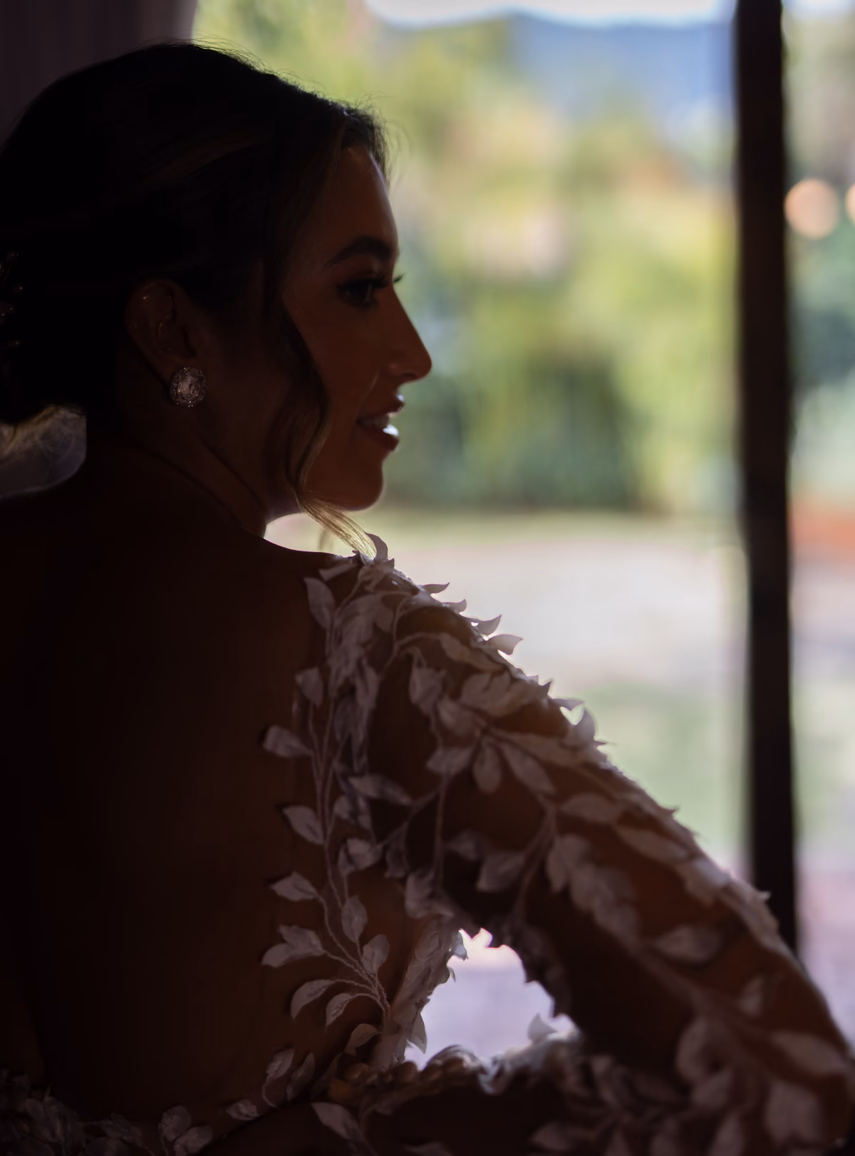 Silueta de Nathaly junto a la ventana, con la luz sobre el encaje de su vestido