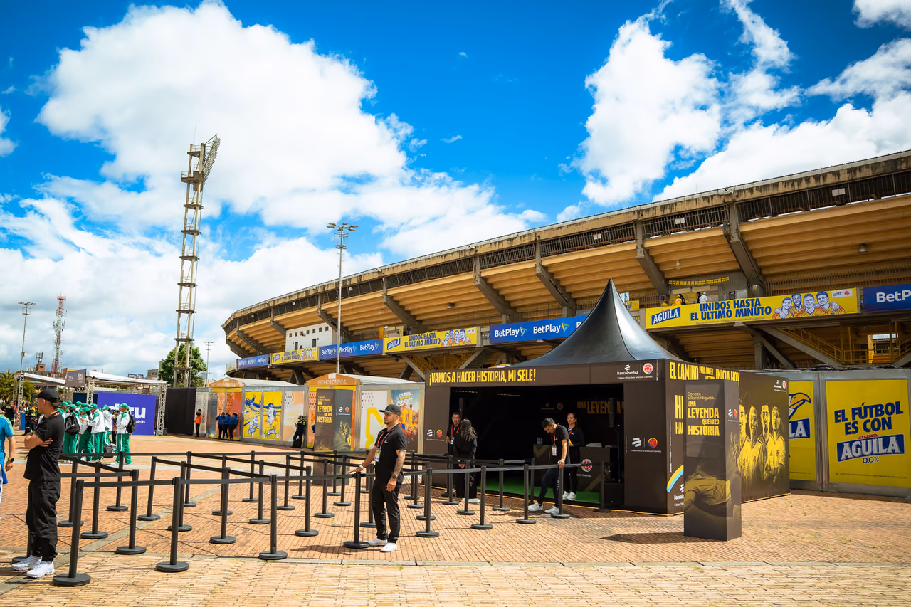 Stand de una activación de marca frente al estadio El Campín en Bogotá, con filas organizadas para el público