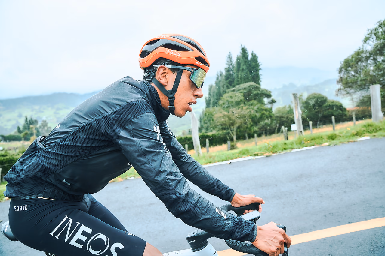 Ciclista profesional con chaqueta de lluvia rueda junto a un embalse