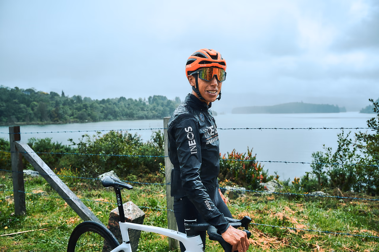 Ciclista profesional sonríe junto a su bicicleta a la orilla de un embalse
