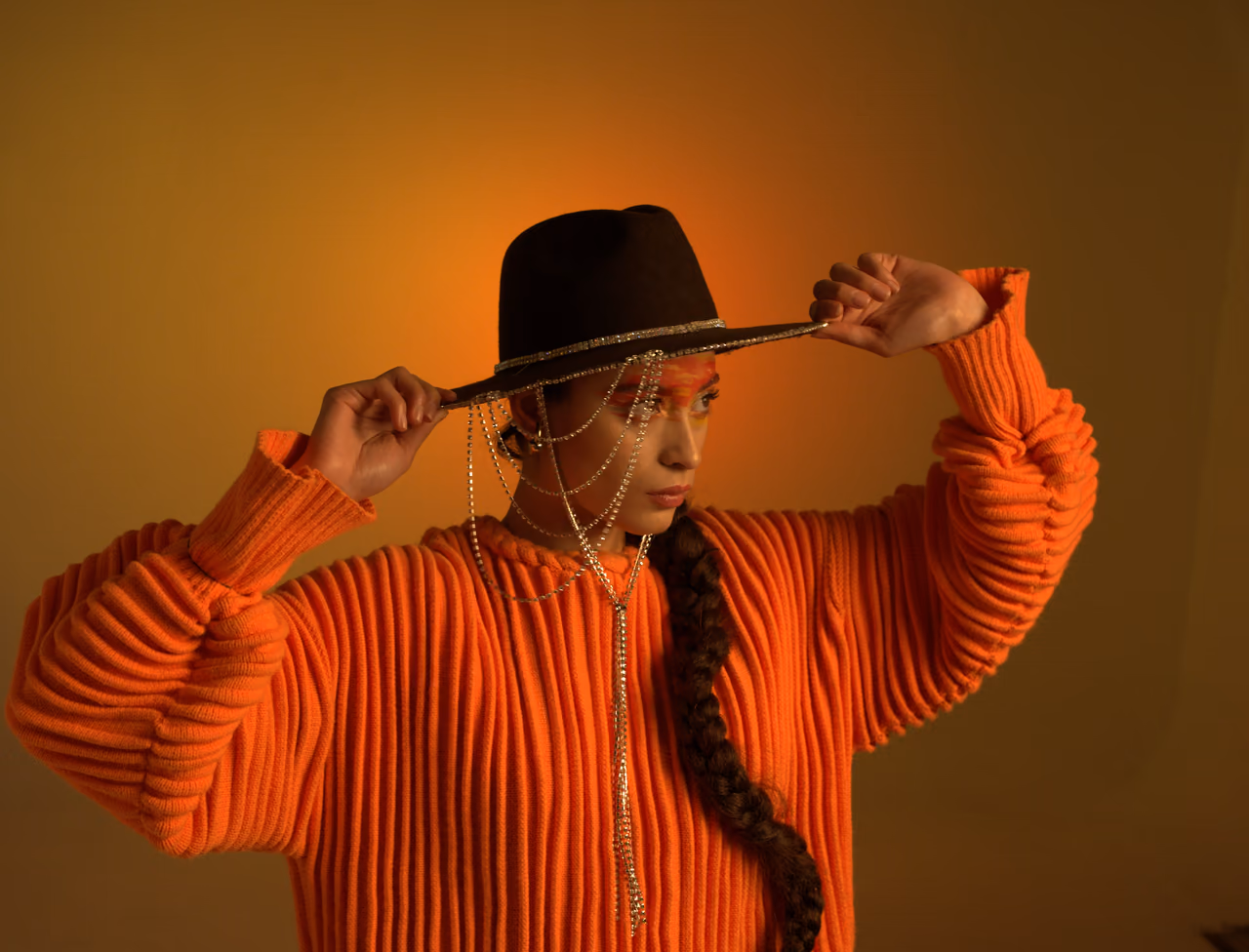 Modelo con sombrero negro y blusa naranja bajo luz cálida en una sesión de Sequoia Studio
