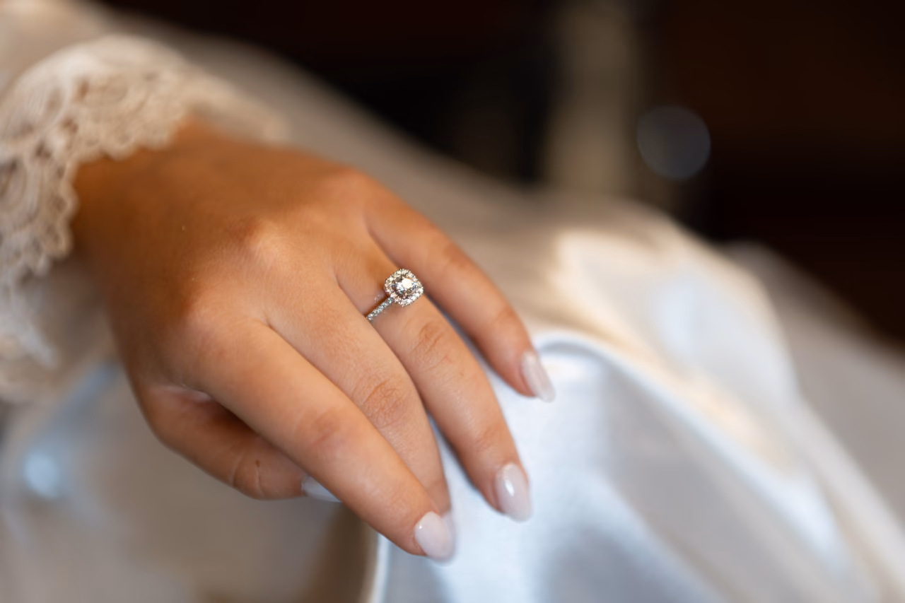 Detalle del anillo de compromiso en la mano de una novia junto al encaje de su vestido