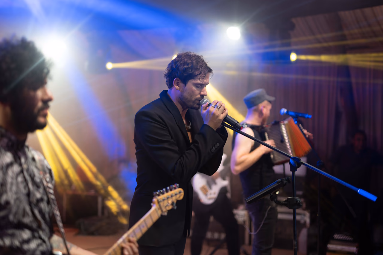 Cantante con micrófono acompañado por guitarrista y acordeonista entre luces azules y amarillas