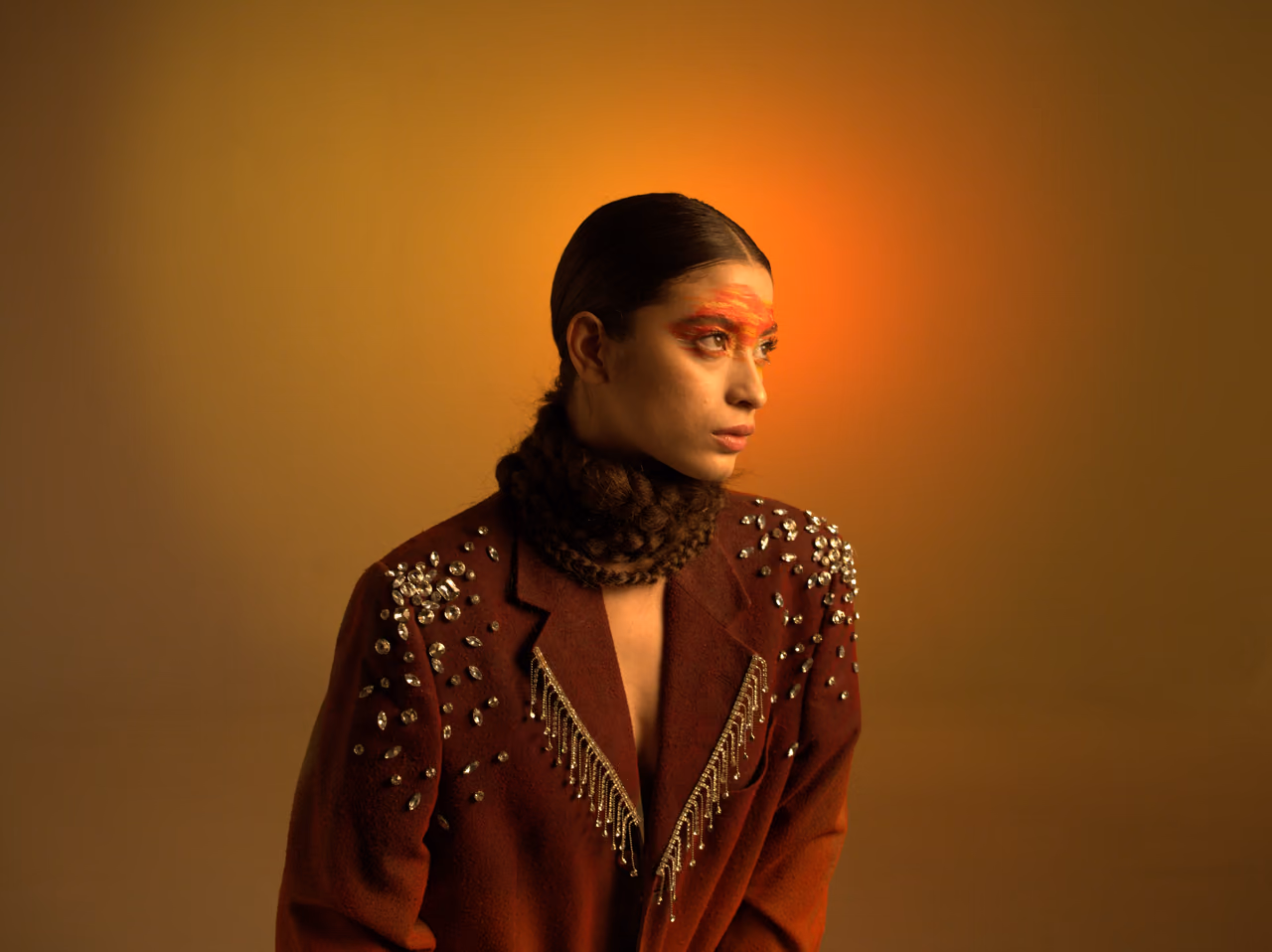 Modelo mirando de perfil con chaqueta marrón bordada bajo luz ámbar