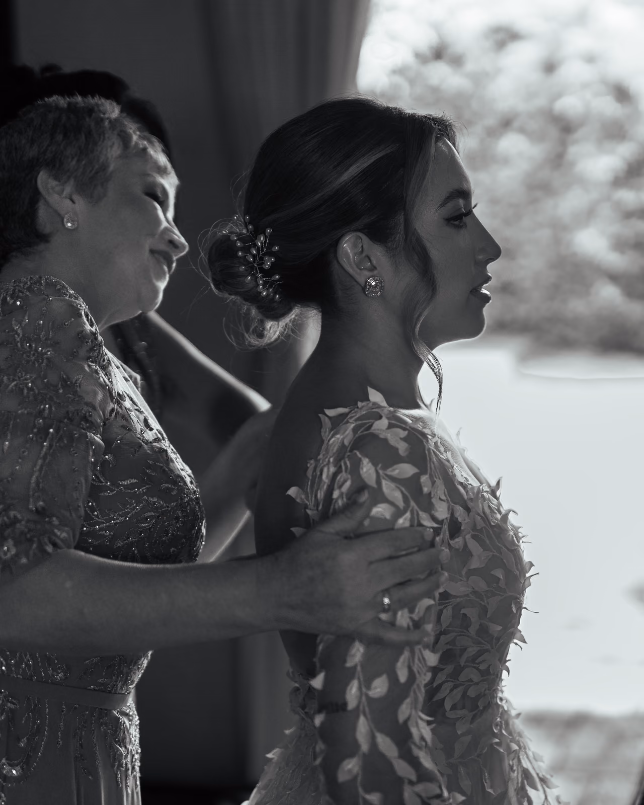 Retrato en blanco y negro de una novia acompañada por una mujer durante sus preparativos